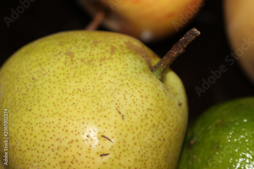 Fresh pear on a dark background surrounded by assorted fruits. Still life composition of fruits. Top view of a rustic organic pear with fruits. Pear with selective focus. Pear on a dark background.