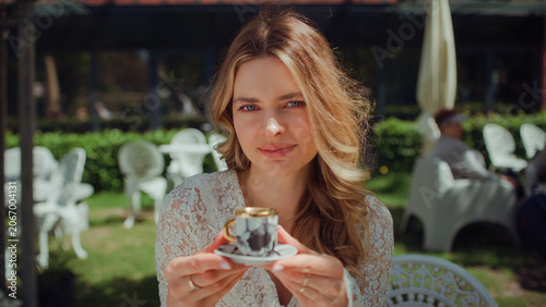 Woman sitting in an outdoor cafe and holding a tiny elegant espresso cup