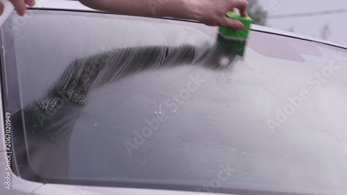 A man washes car windows with detergent before applying anti-rain
