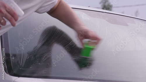 A man washes car windows with detergent before applying anti-rain