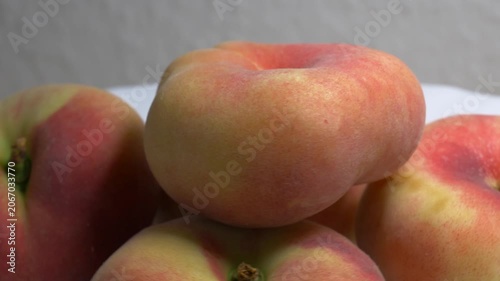 Close-up of a pile of flat donut peaches rotating on a white turntable, showcasing their unique shape and fuzzy skin under bright studio lighting.
