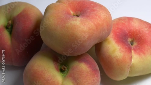 Close-up of a pile of flat donut peaches rotating on a white turntable, showcasing their unique shape and fuzzy skin under bright studio lighting.