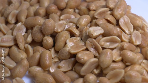 Close-up of roasted peeled peanuts rotating on a white plate, showcasing their smooth texture and golden color under bright studio lighting.