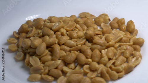 Close-up of roasted peeled peanuts rotating on a white plate, showcasing their smooth texture and golden color under bright studio lighting.