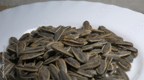 Close-up of a pile of roasted sunflower seeds in shells rotating on a white plate, highlighting their textured surface under bright studio lighting.