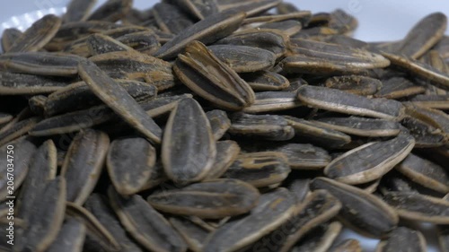 Close-up of a pile of roasted sunflower seeds in shells rotating on a white plate, highlighting their textured surface under bright studio lighting.