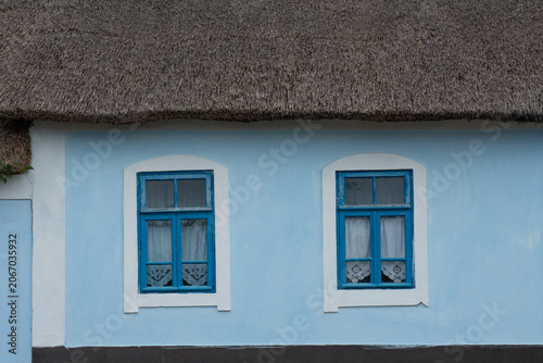 An old clay village house with a thatched roof and wooden shutters. Traditional Ukrainian house.