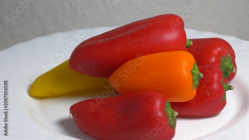 Close-up of fresh red and yellow sweet bell peppers rotating on a white plate, showcasing their smooth texture and vibrant colors under bright studio lighting.