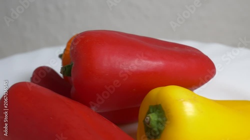 Close-up of fresh red and yellow sweet bell peppers rotating on a white plate, showcasing their smooth texture and vibrant colors under bright studio lighting.