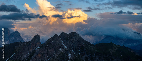 Fotografie Dramatic storm clouds engulf rugged Dolomite mountain peaks at sunset in northern Italy