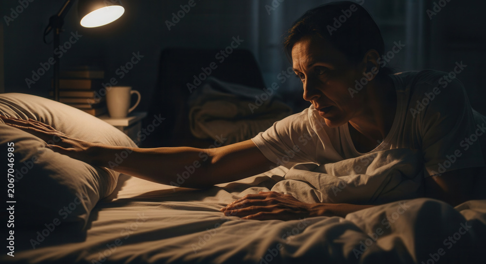 Fototapeta premium Woman Suffering From Insomnia Reaching Out In Bed Under Warm Lamp Lighting