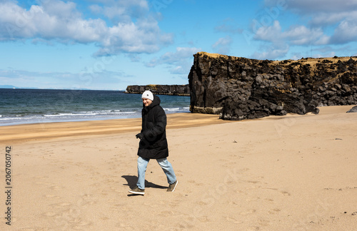 Traveler Walking Along Sandy Volcanic Beach with Basalt Cliffs in Iceland