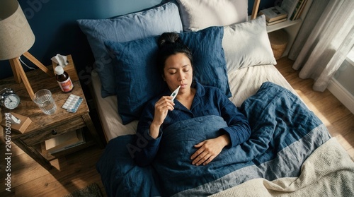 Woman In Bed Taking Temperature With Digital Thermometer During Illness Recovery