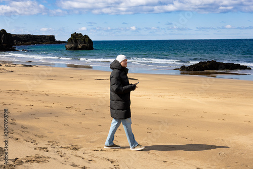 Tourist Standing on Sandy Beach with Atlantic Ocean and Volcanic Rocks in Iceland