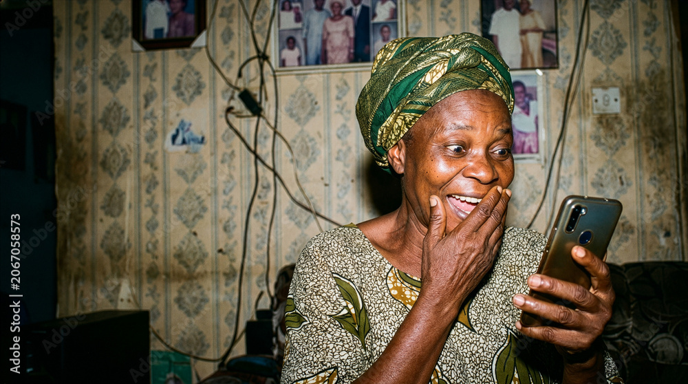 Fototapeta premium Elderly African woman reacts with joy and surprise while looking at her smartphone screen