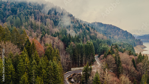 Aerial view of a road through misty autumn forest above a lake, Romania