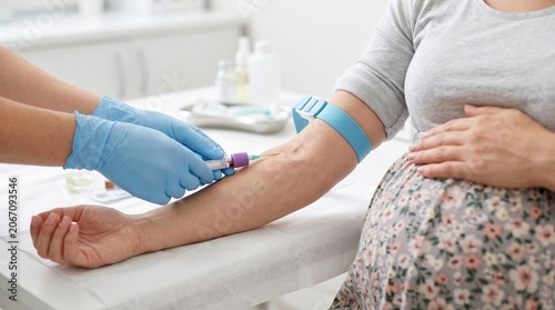 A pregnant woman sits in a clinic while a healthcare worker takes blood from her arm for testing. The atmosphere shows care for health during pregnancy