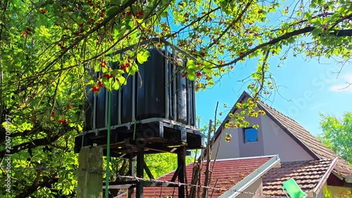 Water tank mounted on wooden structure in green garden setting  