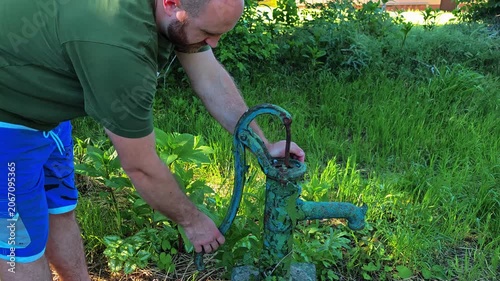 Man operating vintage water pump in garden surrounded by greenery  