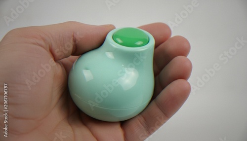 Φωτογραφία A close-up of a person's hand holding a small, mint-green, pear-shaped object with a bright green button on top, suggesting a compact electronic device, fidget toy, or buzzer