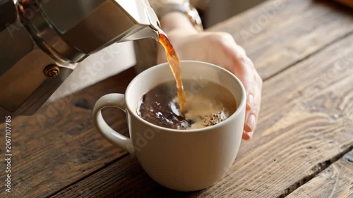 Morning ritual pouring fresh brewed coffee from a stovetop espresso maker into a white mug on rustic wooden table