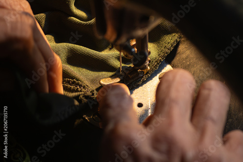 Close up of senior hands carefully guiding a green fabric under the needle of an old vintage sewing machine