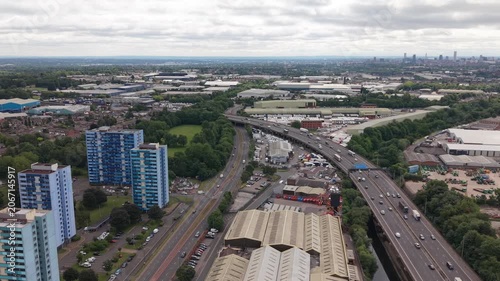 Aerial drone footage showing the M5 motorway passing through industrial estates, residential tower blocks and commercial districts in the West Midlands near Birmingham, England. Urban transport infras