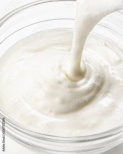 Creamy white yogurt or dairy cream pouring into a glass bowl