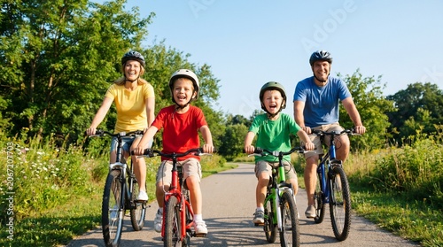 Happy young family of four riding bicycles together on a sunny park trail
