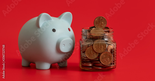 Photography Glass jar with US coins and blue piggy bank on red background