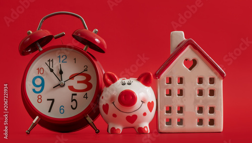 Cuadro en lienzo An alarm clock, a piggy bank, and a symbolic house on a red background