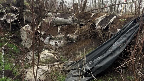 Destroyed military dugout and sandbag trench in a war-damaged forest, checked for explosive items during humanitarian demining. Bleak post-conflict scene
