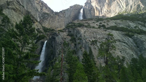 Aerial shot of Yosemite Valley featuring cascading waterfall surrounded by granite cliffs, dense forest, and dramatic mountain landscape in California’s Sierra Nevada.