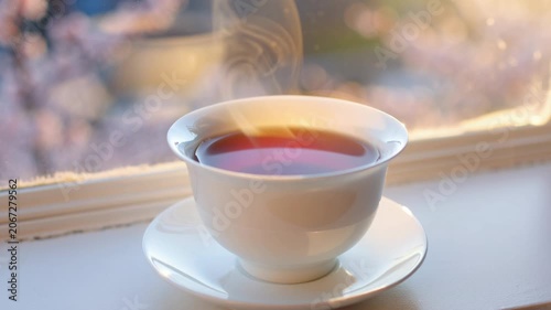 Hot steaming tea in a white cup sitting on a windowsill at sunrise. Seamless looping 4k video background