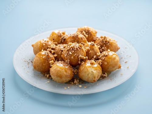 Overhead view of golden loukoumades with honey syrup and walnut topping on frosted glass dish