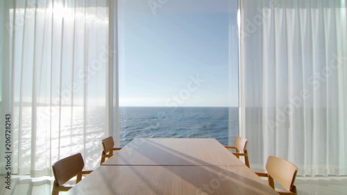 Modern wooden dining table overlooking a calm blue ocean through window. Seamless looping 4k video background