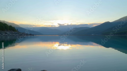 Scenic sunset over calm mountain lake with peaceful nature reflections. Seamless looping 4k video background