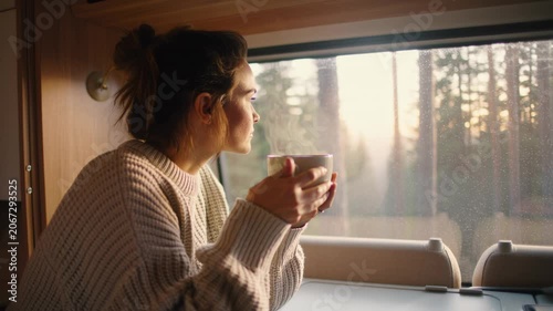 Woman holding a hot steaming mug while traveling inside a cozy camper van. Seamless looping 4k video background