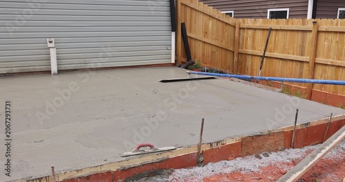 Workers prepare pour concrete for new slab foundation in backyard near garage