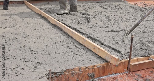 Worker spreads wet concrete for foundation on construction site with wood framing in place.