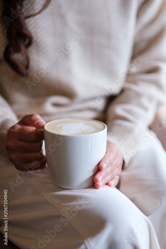 фотографія Vertical closeup image of a woman holding and drinking hot coffee in cafe