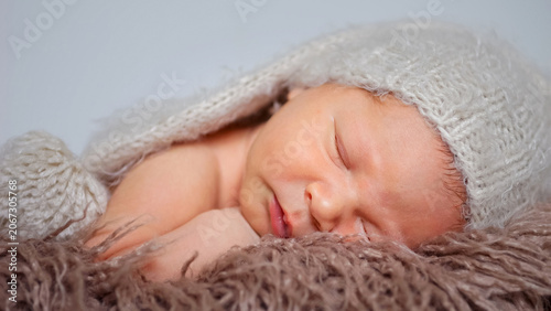 Newborn baby boy sleeping calmly on a fluffy brown blanket, wearing a light grey knitted hat, portraying innocence, comfort, and the serenity of early slumber