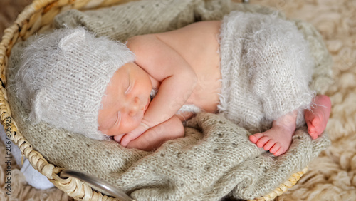 Newborn baby sleeping deeply nestled in a soft woven basket, wearing a cozy knitted hat with ears and matching pants, symbolizing innocence, peace, and new life