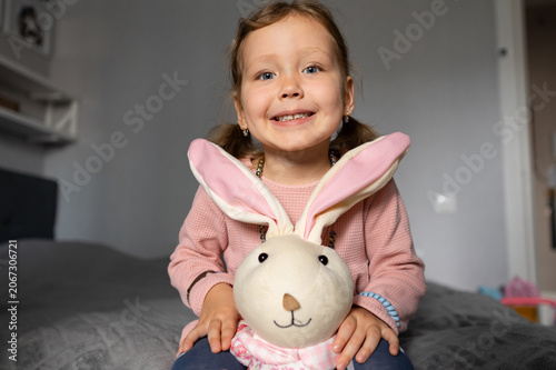 Young child sitting on a bed, expressing genuine joy and happiness while embracing her favorite plush rabbit toy, embodying childhood play