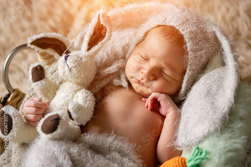 Newborn baby boy sleeping peacefully, wearing a soft bunny hat and nestled amongst a warm blanket, holding a plush rabbit toy, representing innocence and spring