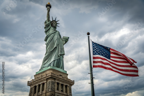 Statue of Liberty with the American flag waving under dramatic cloudy sky for fourth of july independence day celebration patriotic usa landmark views