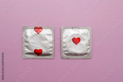 Two condom packets decorated with red hearts on a pastel pink background. Minimal flat lay composition representing safe sex, love, romance, Valentine's Day, sexual health and relationship protection.