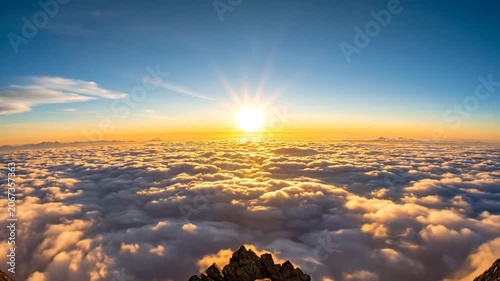 A golden sunrise illuminates the rocky peak above the clouds