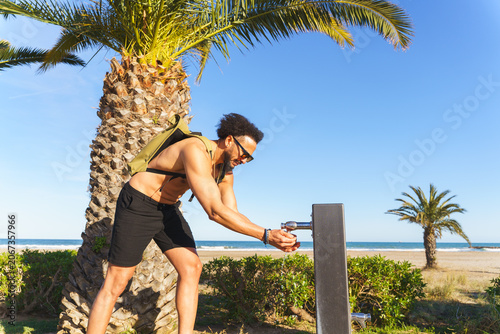 Photography Latino man quenching thirst at a public water fountain during a beach day