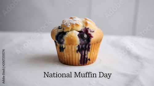 A blueberry muffin with powdered sugar on a marble surface celebrating National Muffin Day